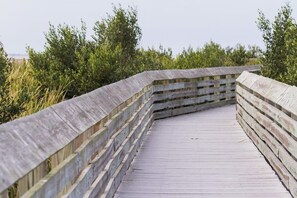 A wooden boardwalk with a curved railing, surrounded by greenery. - Marlin Street Townhome A (South Padre Island)