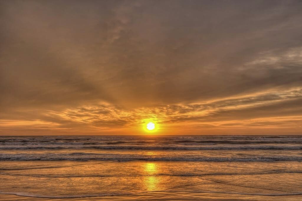 Ein Sonnenuntergang über dem Meer, wobei Wellen den Himmel spiegeln.