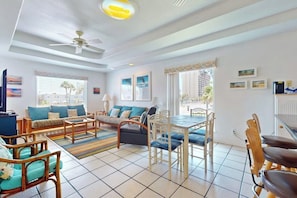 A spacious living area with a sofa set, dining table, and chairs, a ceiling fan, and artwork on the walls. - Marlin Street Townhome A (South Padre Island)