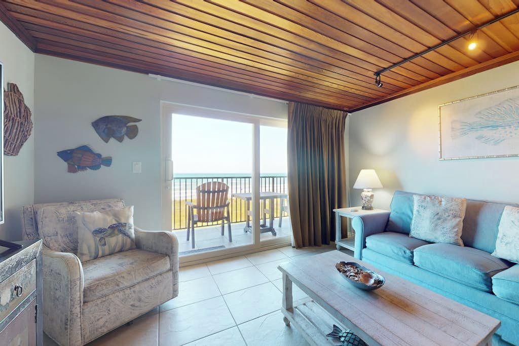 A living room with a wooden ceiling, a sofa, a coffee table, and a balcony with a view.