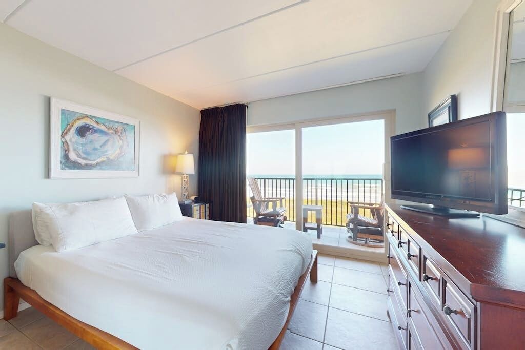 Ein Hotelzimmer mit einem großen Bett, einem Fernseher, einem Gemälde an der Wand und einem Balkon mit Blick.