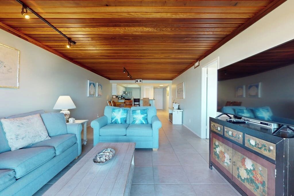 Una sala de estar con techo de madera, un sofá, una mesa de centro y un televisor sobre un mueble.