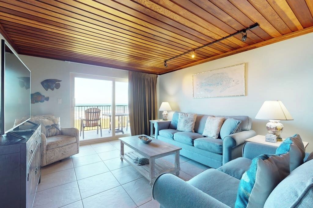 A living room with a wooden ceiling, a sofa set, a coffee table, and a TV.