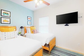 A bedroom with two beds, a ceiling fan, a flat-screen TV, and artwork on the walls. - Star Beachside Condominiums 105 (South Padre Island)