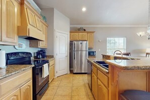 A kitchen with wooden cabinets, a stainless steel refrigerator, a built-in oven, and a granite countertop. - Casa Nirvana - Steps to the Beach & Balcony (South Padre Island)