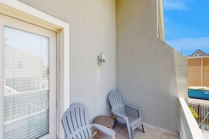 Ein Balkon mit zwei Adirondack-Stühlen, einem kleinen dekorativen Laternen und einem Fenster mit Jalousien.