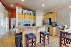 A kitchen with wooden cabinets, a stainless steel refrigerator, a microwave, and a granite countertop. - Casa Nirvana - Steps to the Beach & Balcony (South Padre Island)