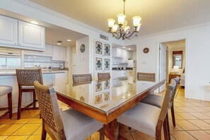 A modern kitchen with white cabinetry, a glass dining table, and a chandelier. - Ocean Vista Condominiums #1101 (South Padre Island)