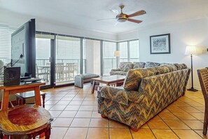 A living room with a sofa, a television, a ceiling fan, and a balcony with a view. - Ocean Vista Condominiums #1101 (South Padre Island)