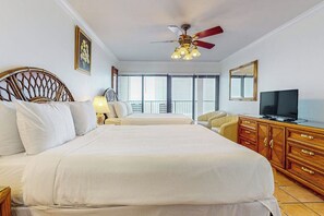 A hotel room with a bed, a desk, a television, and a ceiling fan. - Ocean Vista Condominiums #1101 (South Padre Island)