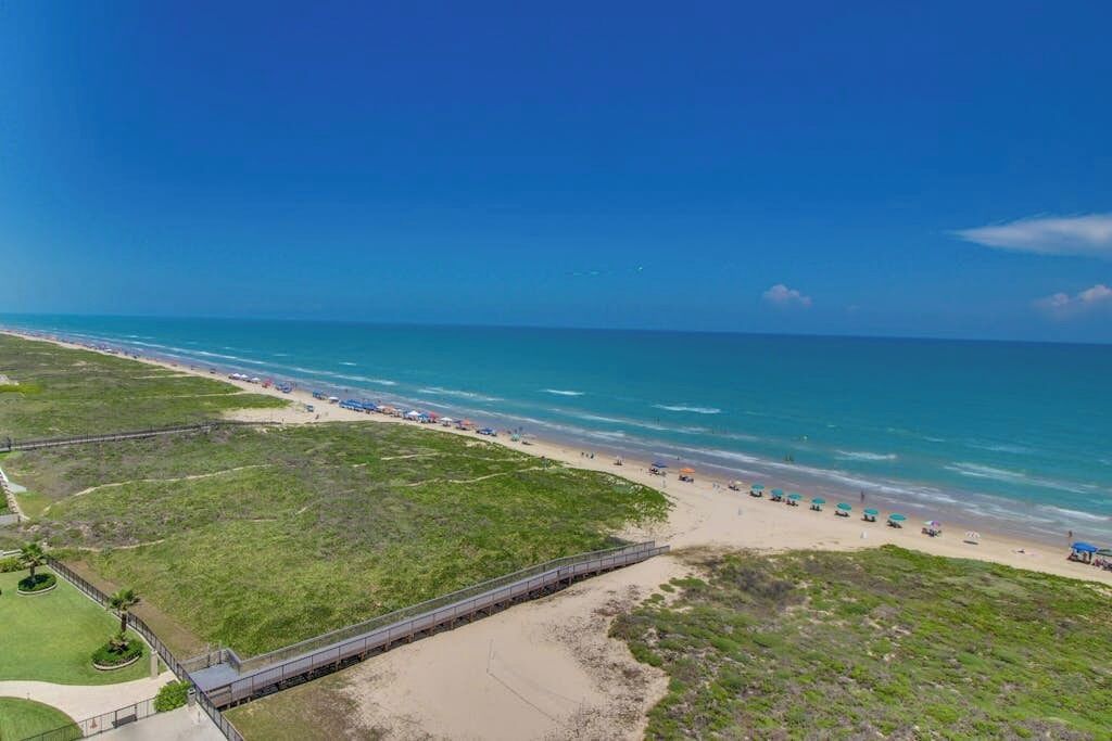 A beach with a long wooden boardwalk leading to the shore, a clear blue sky, and the ocean.