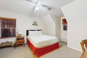 Ein Schlafzimmer mit einem Bett, einem Nachttisch, einer Lampe, einem Deckenventilator und einem Fenster mit Jalousien.