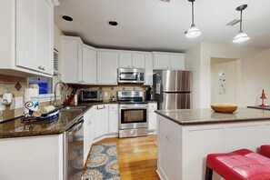 A kitchen with white cabinets, stainless steel appliances, a granite countertop, and a red bench. - The Yellow Pelican - Bay Views, Steps to the Sand (Jamaica Beach)
