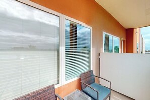A balcony with a glass door, a chair, and a table. - La Isla Condominiums #F304 (South Padre Island)