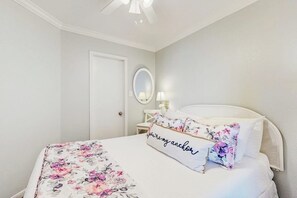 Ein Schlafzimmer mit Bett, Nachttisch, Spiegel und Deckenventilator.