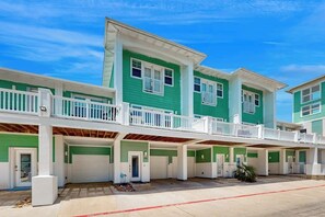 A multi-story residential building with a green facade, white railings, and a covered parking area. - The Meridian Unit 14 (Port Aransas)