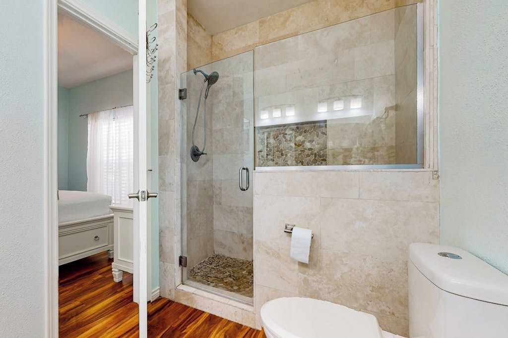 A bathroom with a glass-enclosed shower, a toilet, and a wooden floor.
