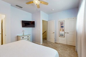 A bedroom with a bed, a ceiling fan, a television, and a set of white doors. - The Meridian Unit 14 (Port Aransas)