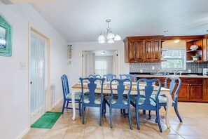 A dining area with a wooden table and blue chairs, a kitchen with wooden cabinets, and a green doormat. - Family Tides - Game Room, Steps to the Water (Port Isabel)