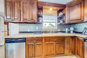 A kitchen with wooden cabinets, a dishwasher, and a window with a view. - Family Tides - Game Room, Steps to the Water (Port Isabel)