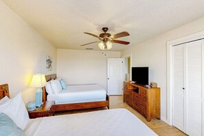 Ein Schlafzimmer mit zwei Betten, einem Deckenventilator, einer Kommode, einem Fernseher und einer Tür.