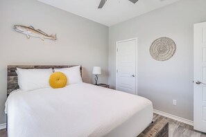A bedroom with a bed, a nightstand, a wall-mounted lamp, a door, and a wall decoration. - The Bay Breeze Beauty (Corpus Christi)