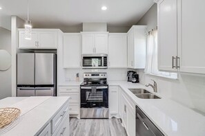 A modern kitchen with white cabinetry, stainless steel appliances, and a marble countertop. - The Bay Breeze Beauty (Corpus Christi)