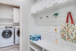 A laundry room with a washing machine, a drying rack, and a bench with folded clothes. - The Bay Breeze Beauty (Corpus Christi)