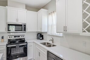 Una cocina moderna con armarios blancos, un microondas integrado, una estufa y un lavabo.