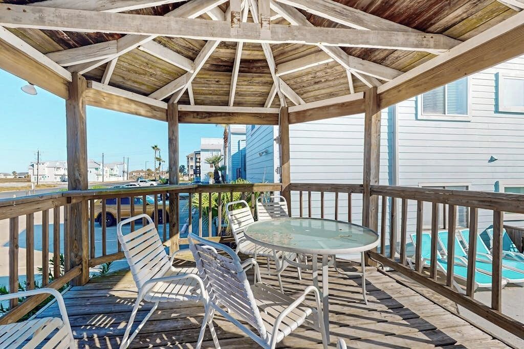 A covered outdoor seating area with metal chairs and a glass table, overlooking a swimming pool.