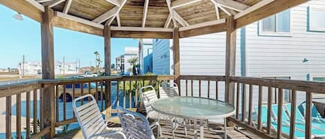 A covered outdoor seating area with metal chairs and a glass table, overlooking a swimming pool.