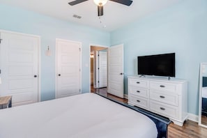 A bedroom with a bed, a TV, a dresser, and a ceiling fan. - The Blue Shell - Pool, Big Deck & Dog-Friendly (Port Aransas)