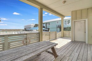 Un espace extérieur abrité, doté d’un banc en bois, d’une porte et offrant une vue sur des maisons en arrière-plan.