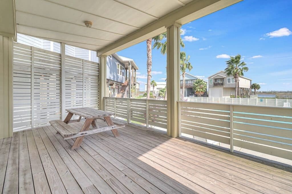 A covered outdoor area with a wooden deck, a picnic table, and a view of neighboring houses.