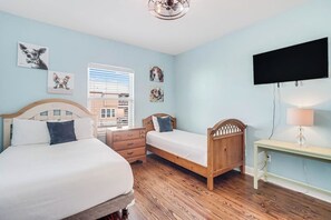 Une chambre avec deux lits, une tête de lit en bois, une table de chevet, un téléviseur fixé au mur et une fenêtre avec des stores.