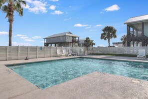 A swimming pool with lounge chairs, a wooden fence, and a building with a balcony. - The Blue Shell - Pool, Big Deck & Dog-Friendly (Port Aransas)