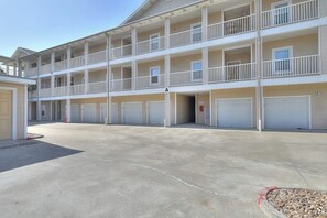 A multi-story building with balconies, a parking area, and garage doors. - Compass Condominiums A7 (Corpus Christi)
