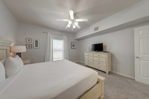 Ein Schlafzimmer mit Bett, Kommode, Fernseher und Deckenventilator.