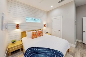 A bedroom with a bed, bedside tables, a window, and a door. - Martinis & Marlin - Heated Pool (Port Aransas)