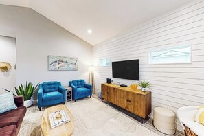 A modern living room with a flat-screen TV, two blue armchairs, a wooden cabinet, and a coffee table. - Martinis & Marlin - Heated Pool (Port Aransas)