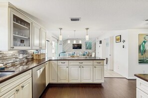 A kitchen with a central island, white cabinetry, and a herringbone-patterned backsplash. - Lost Colony Laidback Hideaway (Port Aransas)