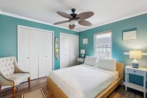 Ein Schlafzimmer mit Bett, Stuhl, Deckenventilator, Fenster und Tür.