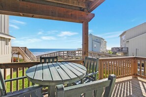Eine Holzterrasse mit Tisch und Stühlen, die auf einen Strand und Gebäude blickt.