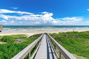 A wooden boardwalk leading to a beach with a clear sky and ocean view. - Lost Colony Laidback Hideaway (Port Aransas)