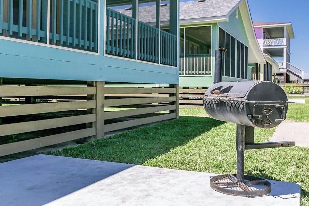 A barbecue grill on a concrete pad in front of a building with a green exterior and a wooden fence.