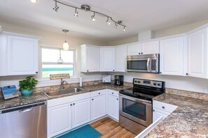 A modern kitchen with white cabinets, stainless steel appliances, and a granite countertop. - Rockport Getaway - Screened Porch, Near the Beach (Rockport)