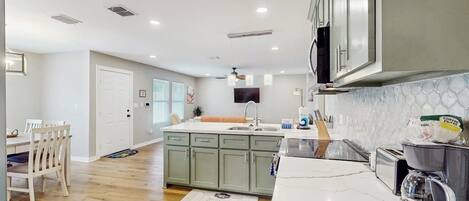 Una cocina moderna con una isla central, un comedor con sillas y vista al salón.