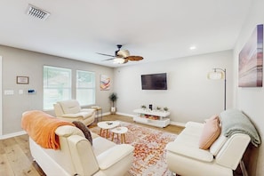 A modern living room with a sofa, armchairs, a coffee table, a TV, and a ceiling fan. - Emerald Escape - Steps to the Sand, Near Downtown (Corpus Christi)