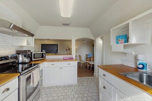 A modern kitchen with white cabinetry, a microwave, a stove, and a sink. There is a dining area with a table and chairs visible in the background. - El Cerrito Place - Unit B (Port Aransas)