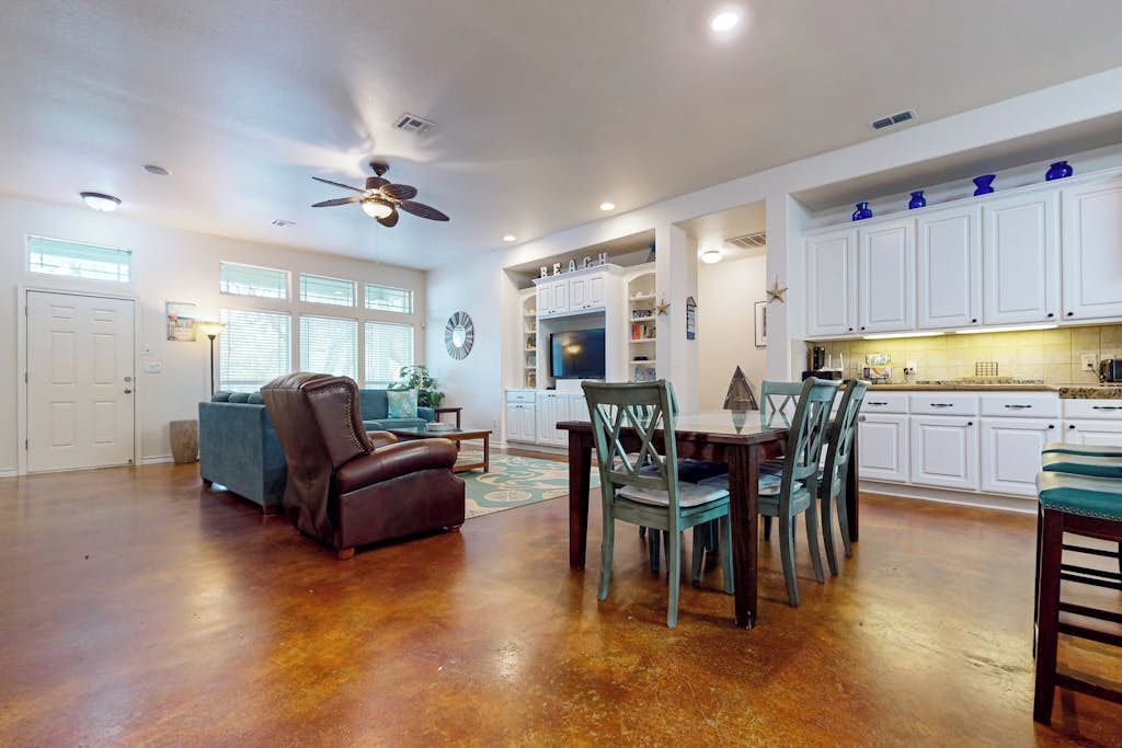 A spacious living area with a dining table, chairs, a sofa, and a ceiling fan.